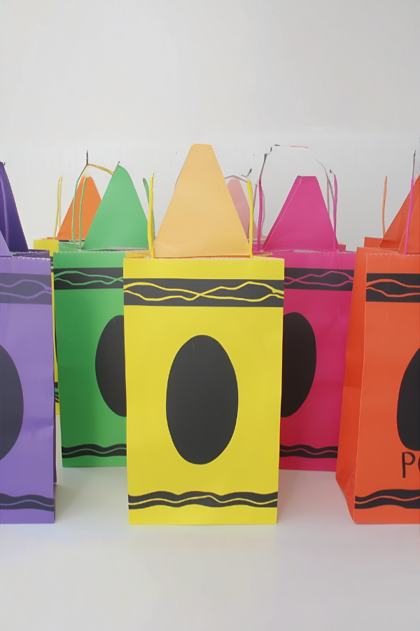 Colorful DIY party favor bags shaped like oversized crayons with black name labels.