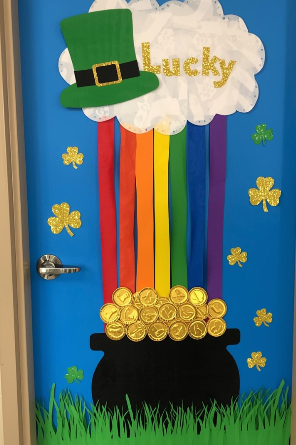 St. Patrick’s Day door decoration with a rainbow flowing from a cloud into a pot of gold, green leprechaun hat, shamrocks, and “Lucky” sign on a blue background