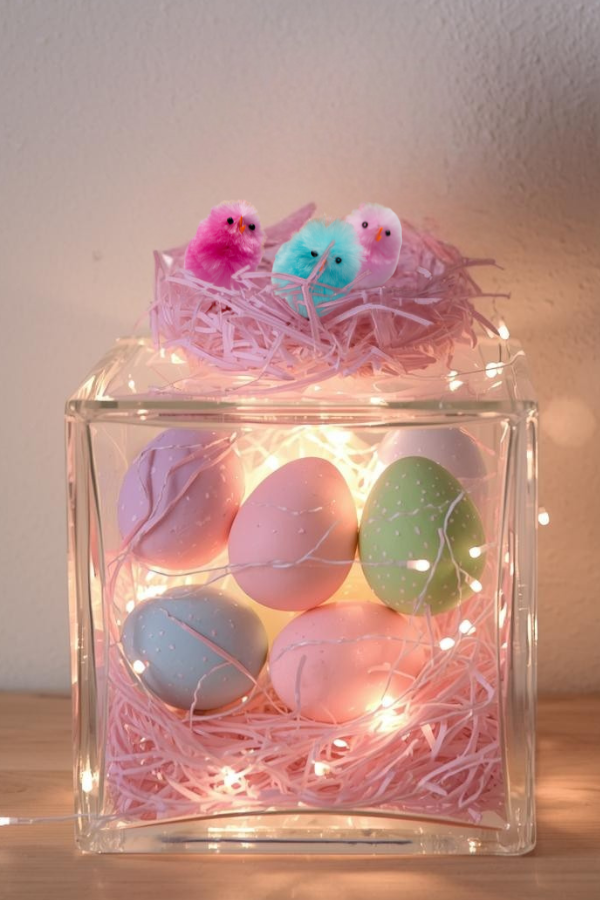 Easter chicks on glass container filled with pastel eggs and lights