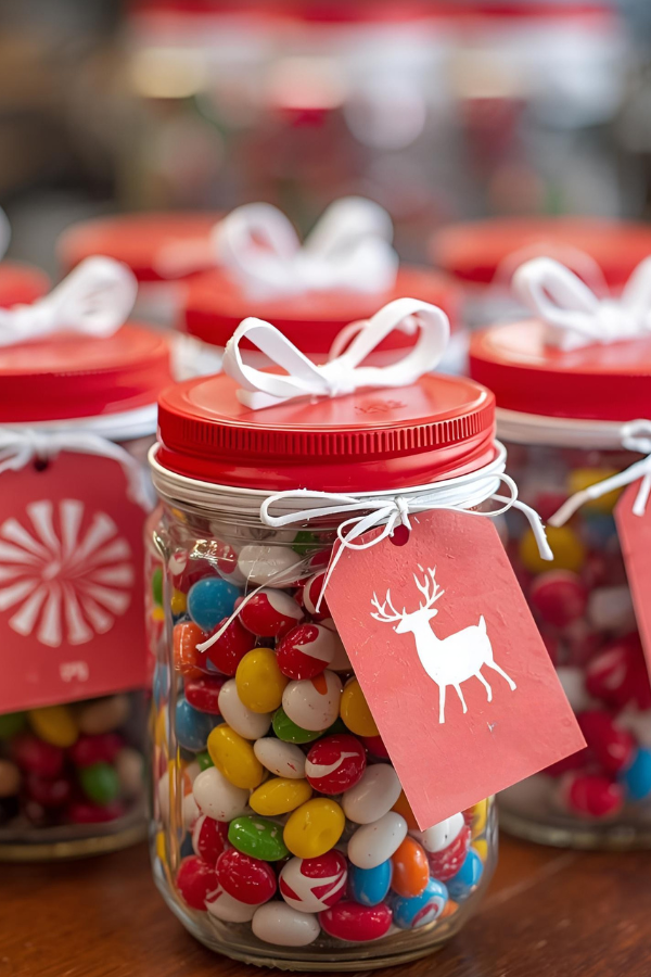 Festive snack jars filled with colorful Christmas candies, decorated with red lids, curly ribbon, and holiday labels on an office desk.