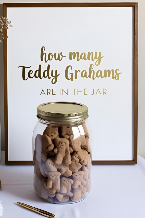 Glass jar filled with Teddy Grahams in front of a framed sign that reads 'How many Teddy Grahams are in the jar,' set on a table with a gold pen beside it.