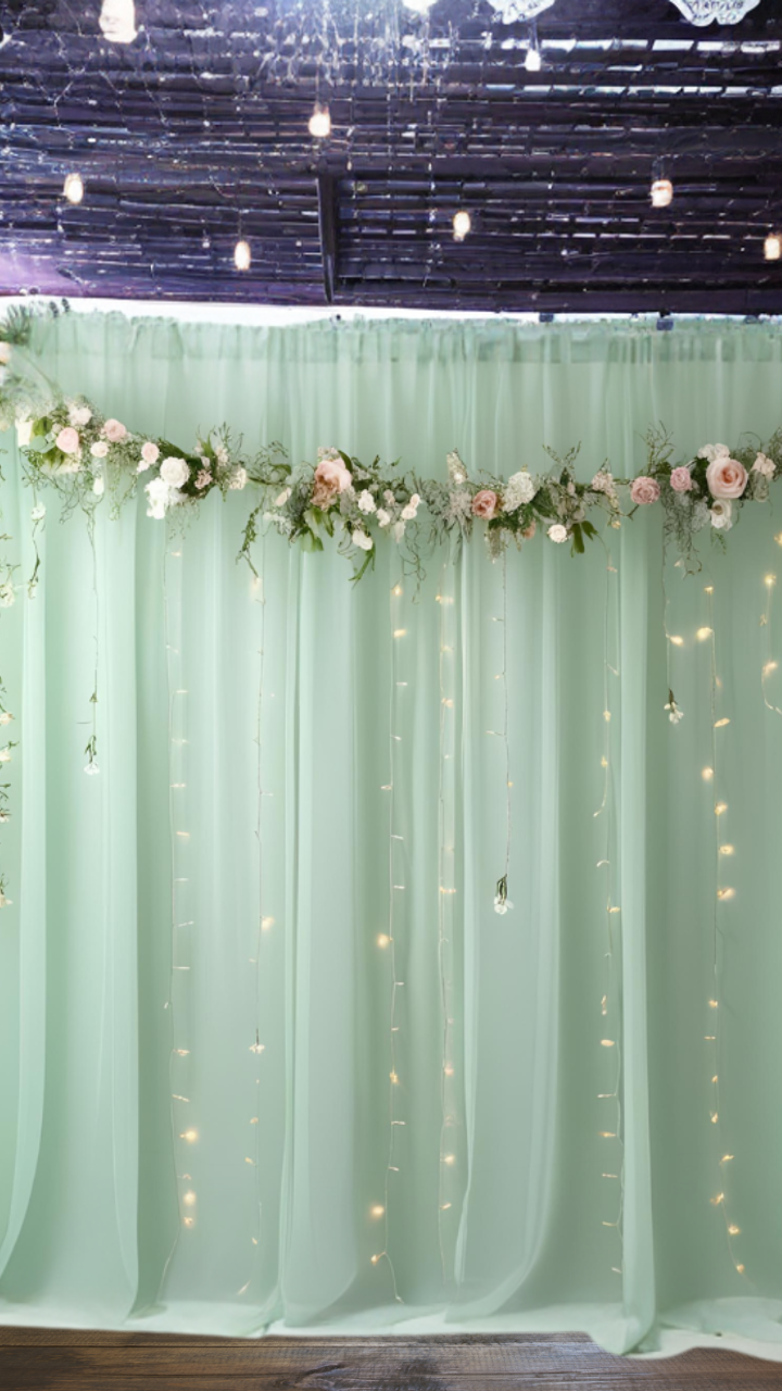 Enchanted forest-themed bridal shower backdrop with soft green drapery, floral garland, and twinkling fairy lights