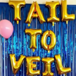 Mermaid bridal shower backdrop with gold balloon letters spelling 'Tail to Veil' against blue shimmering streamers, with a pink balloon decoration