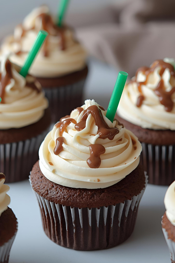 Chocolate cupcakes topped with swirled creamy frosting, drizzled with mocha sauce, and finished with small green drink straws for a café-inspired look.