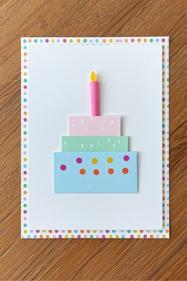 Handmade birthday card with a flat layered paper cake in pastel colors and a polka dot border.