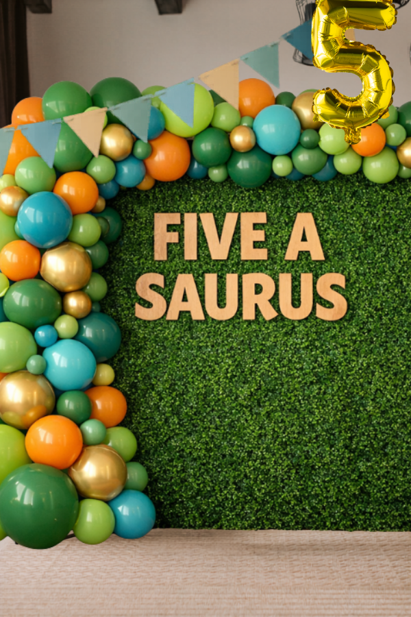 Green hedge wall with colorful balloon garland and “Five A Saurus” sign