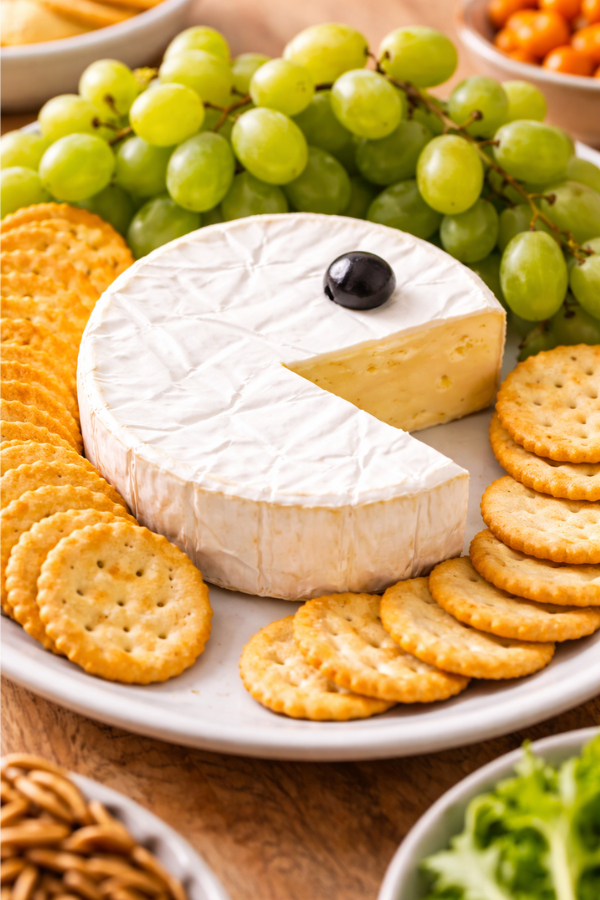 Brie cheese shaped like a retro arcade character with grapes and crackers