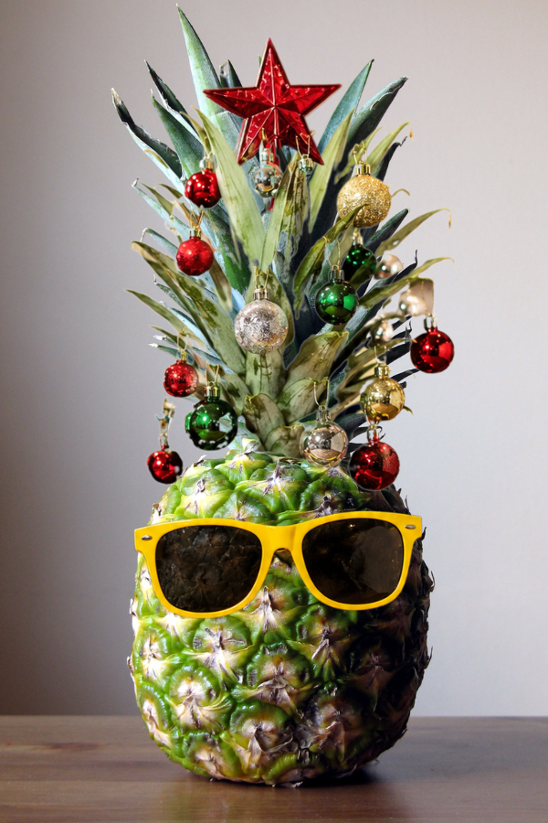 Pineapple decorated with sunglasses, ornaments, and star toppers as a tropical Christmas in July centerpiece.
