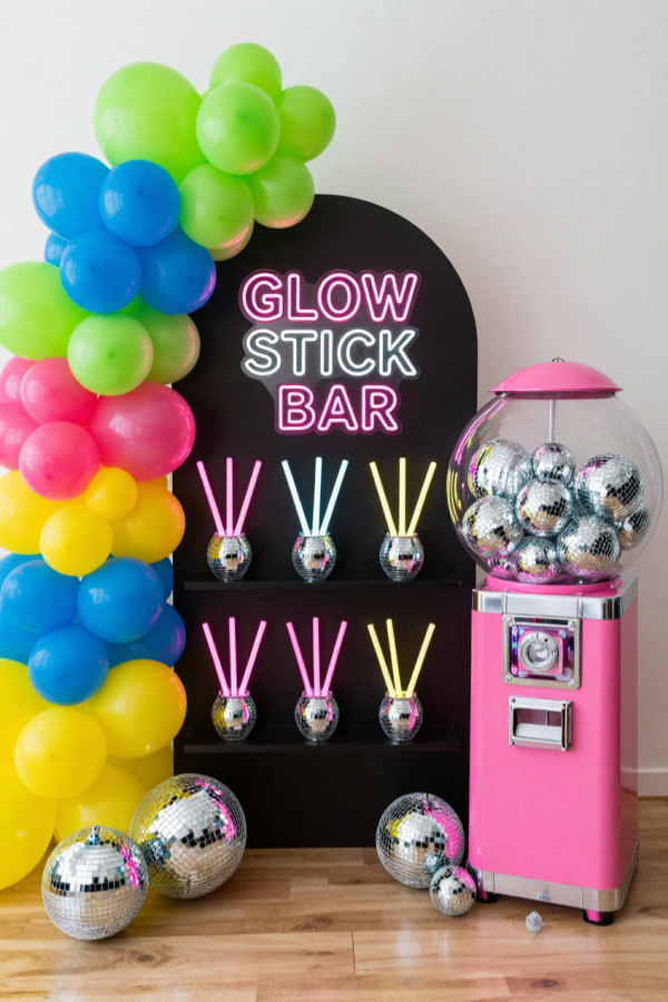 Neon glow stick bar with disco ball planters, colorful balloons and a pink gumball machine filled with disco balls.